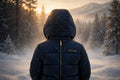 Enfant de dos, capuche relevée, portant la doudoune d'hiver DULUXE bleu nuit et jouant dans la neige, présentation premium noir et doré