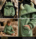 Enfant souriant portant la Combinaison Polaire Douillette DULUXE verte motif monstre avec capuche à cornes douces, dans un salon chaleureux