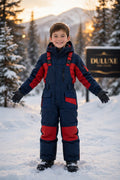 Enfant souriant en salopette de neige marine et rouge dans un paysage hivernal canadien, visuel principal DULUXE