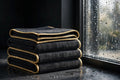 Chiffons microfibre grand format DULUXE empilés près d'une fenêtre étincelante, présentation premium noir et doré